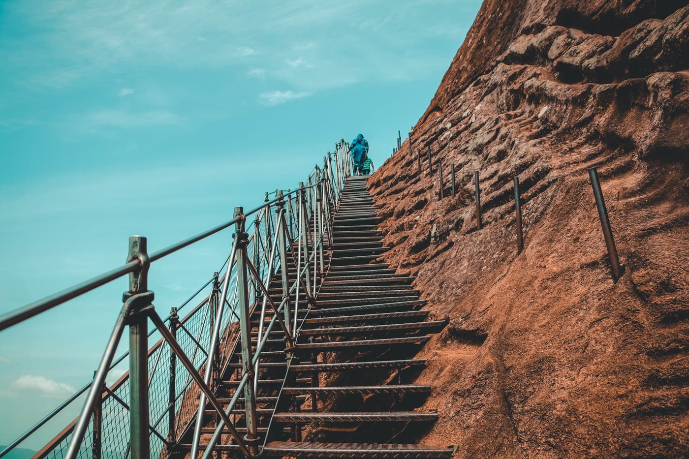 A metal stairway with handrails running along the orange rock face of Sigiriya