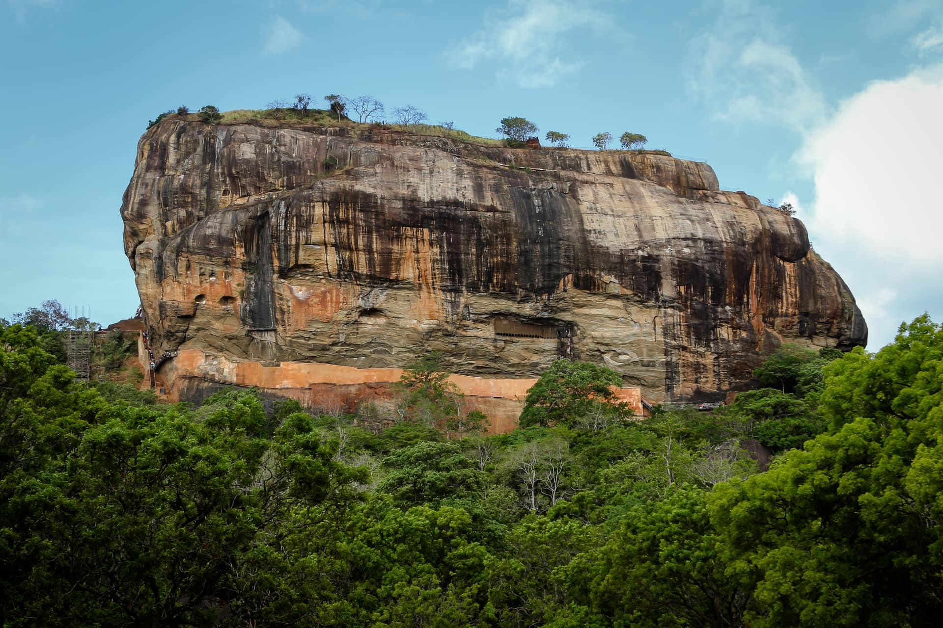 The sheer orange and grey walls of Sigiriya rock rising above the green forest canopy