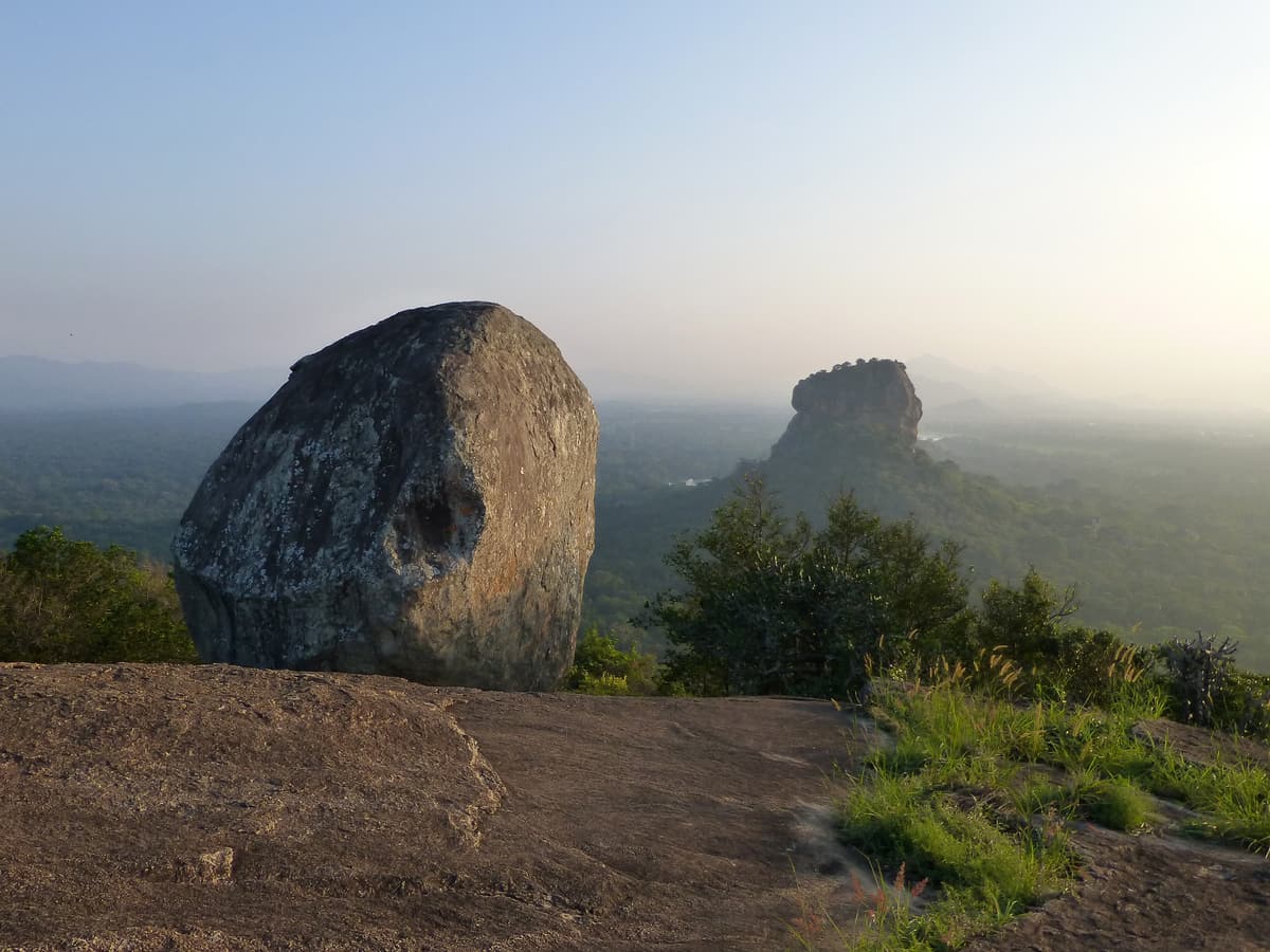 A huge boulder on top of Pidurangala with Sigiriya rock rising from the forest behind it